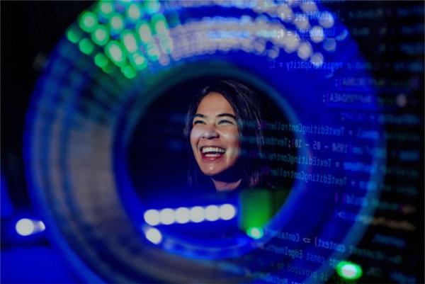 A college student smiles as seen through a round blue and green shape with computer coding double exposed. 