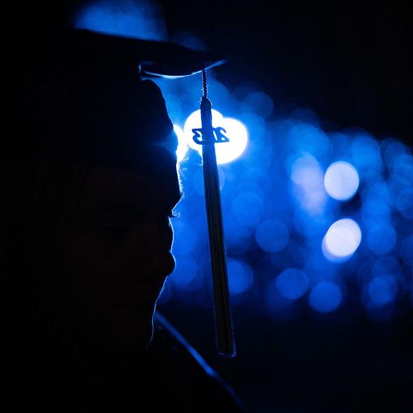A person wearing a cap and gown is illuminated by blue lights.