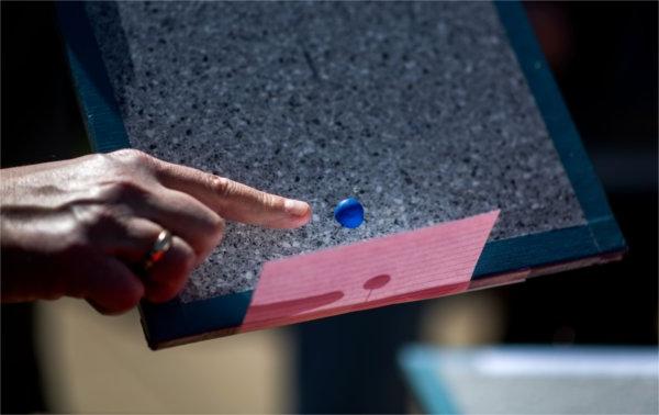 The index finger on a person's hand points to a small blue ball next to a pink card.